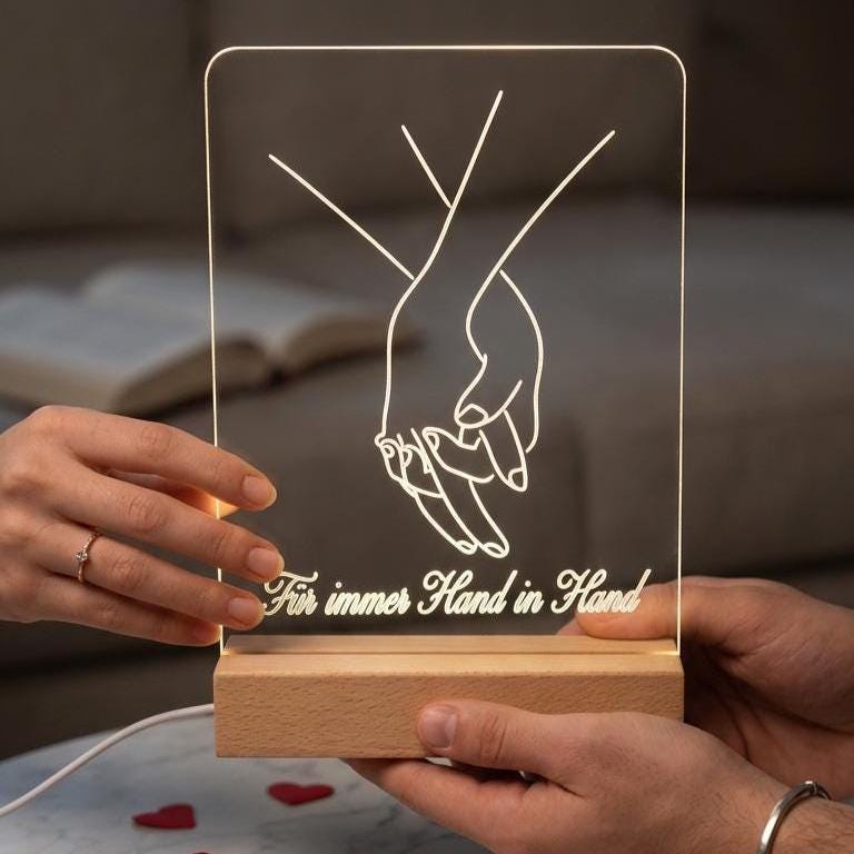Zwei Personen halten eine leuchtende Händemotiv-Lampe mit Schriftzug Für immer Hand in Hand